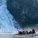 Group of people paddling a canoe on calm water near a cascading waterfall surrounded by rocky cliffs